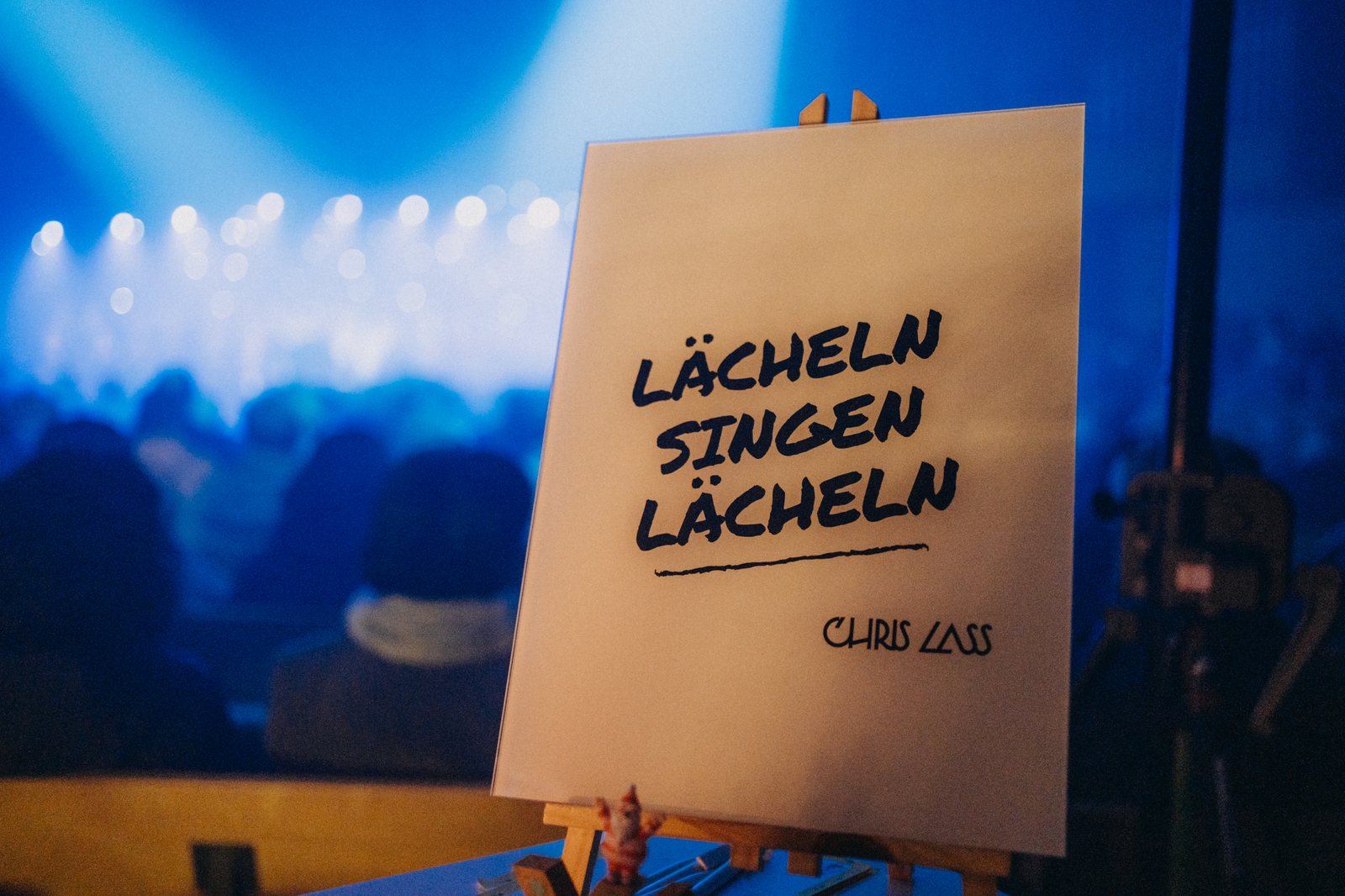 Schild auf der Bühne: Lächeln, Singen, Lächeln — Chris Lass